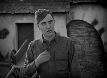 Movie still from “The Big Parade” (1925), directed by King Vidor – A man in a military uniform is standing in front of a building; Medium shot, High angle