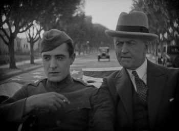 Movie still from “The Big Parade” (1925), directed by King Vidor – A man and a man in a hat and a car in the background; Medium shot, Low angle