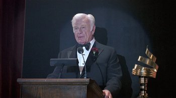 Movie still from “The Big Picture” (1989), directed by Christopher Guest – An older man in a tuxedo speaking at a podium; Medium shot, Low angle