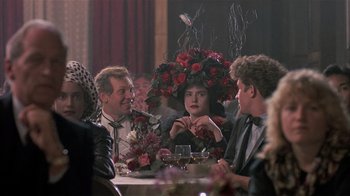 Movie still from “The Big Picture” (1989), directed by Christopher Guest – A group of people sitting at a table with flowers on their heads; Medium shot, Over the shoulder angle