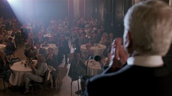 Movie still from “The Big Picture” (1989), directed by Christopher Guest – A group of people sitting at tables in a room; Wide shot, Over the shoulder angle