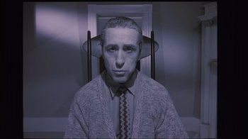Movie still from “The Big Picture” (1989), directed by Christopher Guest – A man in a sweater and tie is sitting in front of a chair; Medium shot, Low angle