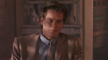 Movie still from “The Big Picture” (1989), directed by Christopher Guest – A man wearing a suit and tie sitting in front of a painting; Close Up shot, Over the shoulder angle