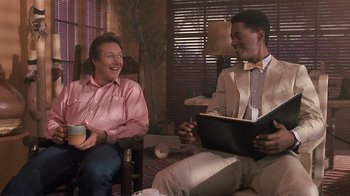 Movie still from “The Big Picture” (1989), directed by Christopher Guest – Two men are sitting in a living room and one is holding a book; Medium shot, Over the shoulder angle