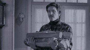 Movie still from “The Big Picture” (1989), directed by Christopher Guest – A man holding a piece of wood while wearing a hat; Medium shot, Low angle