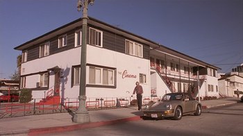 Movie still from “The Big Picture” (1989), directed by Christopher Guest – A man standing in front of a building next to a car; Wide shot, Low angle