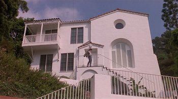 Movie still from “The Big Picture” (1989), directed by Christopher Guest – A man holding an umbrella while standing on the steps of a house; Extreme Wide shot, Low angle