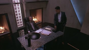 Movie still from “The Big Picture” (1989), directed by Christopher Guest – Two men sitting at a table in front of a fireplace; Wide shot, High angle