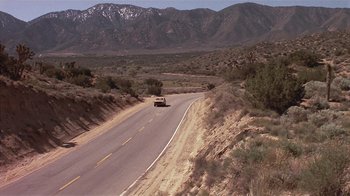 Movie still from “The Big Picture” (1989), directed by Christopher Guest – A car driving down a road in the middle of the desert; Extreme Wide shot, High angle