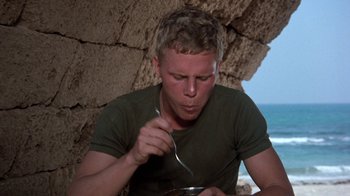 Movie still from “The Big Red One” (1980), directed by Samuel Fuller – A man eating something while sitting on the beach; Close Up shot, Low angle