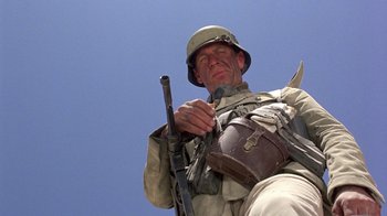 Movie still from “The Big Red One” (1980), directed by Samuel Fuller – A man holding a rifle while standing on top of a building; Close Up shot, Low angle