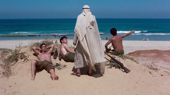 Movie still from “The Big Red One” (1980), directed by Samuel Fuller – A group of men sitting on top of a sandy beach next to the ocean; Wide shot, Over the shoulder angle