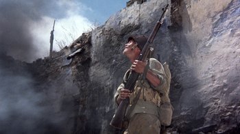 Movie still from “The Big Red One” (1980), directed by Samuel Fuller – A man holding a rifle in front of a rock wall; Medium shot, Low angle