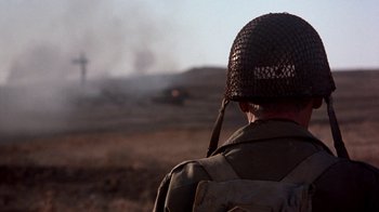 Movie still from “The Big Red One” (1980), directed by Samuel Fuller – A man wearing a helmet looking out at a smoke filled sky; Medium shot, Over the shoulder angle