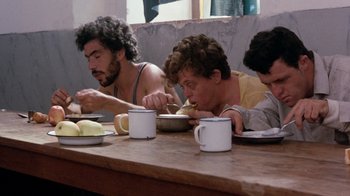 Movie still from “The Big Red One” (1980), directed by Samuel Fuller – A group of men sitting at a wooden table eating food; Medium shot, Low angle