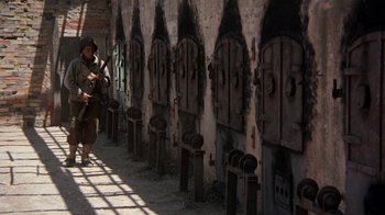 Movie still from “The Big Red One” (1980), directed by Samuel Fuller – A man walking down a street past a row of doors; Wide shot, High angle