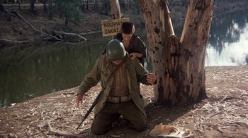 Movie still from “The Big Red One” (1980), directed by Samuel Fuller – A man kneeling down next to a tree while another kneeling down next to a tree; Wide shot, High angle