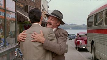 Movie still from “The Big Town” (1987), directed by Harold Becker – A man in a suit and a hat hugging another man; Medium shot, Over the shoulder angle