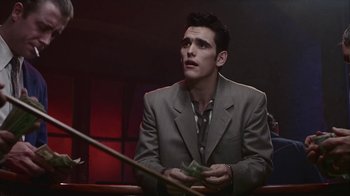 Movie still from “The Big Town” (1987), directed by Harold Becker – A man sitting at a table with a dollar bill in his hands; Medium shot, Low angle