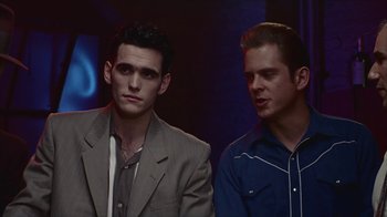 Movie still from “The Big Town” (1987), directed by Harold Becker – Two young men are sitting next to each other; Medium shot, Low angle