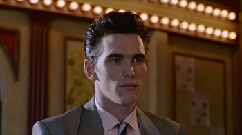 Movie still from “The Big Town” (1987), directed by Harold Becker – A man in a suit and tie in front of lights; Close Up shot, Low angle