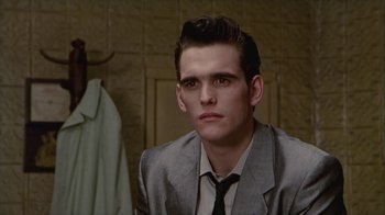 Movie still from “The Big Town” (1987), directed by Harold Becker – A man in a suit and tie sitting in front of a wall; Close Up shot, Low angle