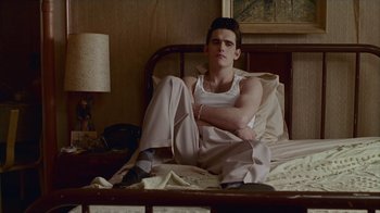 Movie still from “The Big Town” (1987), directed by Harold Becker – A man sitting on a bed in a room; Medium shot, High angle