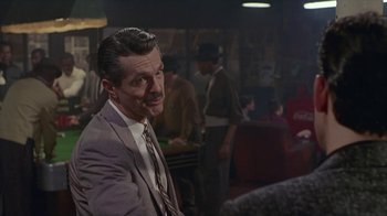 Movie still from “The Big Town” (1987), directed by Harold Becker – A man wearing a suit and tie in a room; Medium shot, Over the shoulder angle