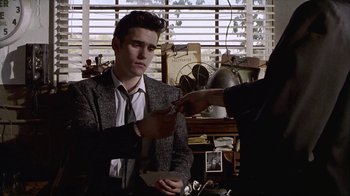 Movie still from “The Big Town” (1987), directed by Harold Becker – A man in a suit and tie holding a piece of paper in his hand; Medium shot, Over the shoulder angle