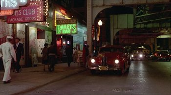 Movie still from “The Big Town” (1987), directed by Harold Becker – A car is parked on the side of the street; Wide shot, High angle