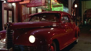 Movie still from “The Big Town” (1987), directed by Harold Becker – An old car is parked on the side of the street; Wide shot, Low angle