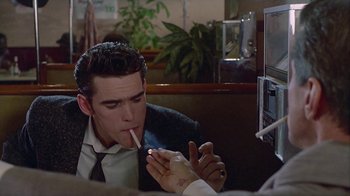 Movie still from “The Big Town” (1987), directed by Harold Becker – A man smoking a cigarette in front of a computer screen; Medium shot, Over the shoulder angle
