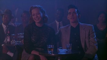 Movie still from “The Big Town” (1987), directed by Harold Becker – A man and a woman sitting at a table with drinks in front of them; Medium shot, Low angle