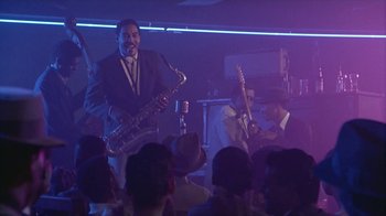Movie still from “The Big Town” (1987), directed by Harold Becker – A group of men playing musical instruments on a stage; Wide shot, Low angle