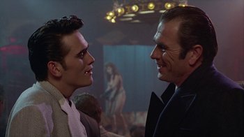 Movie still from “The Big Town” (1987), directed by Harold Becker – Two men in suits talking to each other in front of a crowd; Close Up shot, Over the shoulder angle