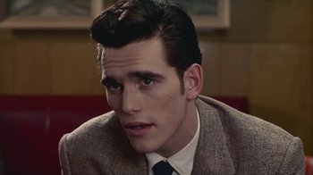 Movie still from “The Big Town” (1987), directed by Harold Becker – A man in a suit and tie sitting in a room; Close Up shot, Over the shoulder angle