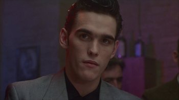 Movie still from “The Big Town” (1987), directed by Harold Becker – A man in a suit and tie looking at the camera; Close Up shot, Low angle