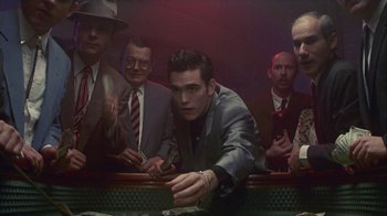 Movie still from “The Big Town” (1987), directed by Harold Becker – A group of men standing around a table with money; Medium shot, Low angle