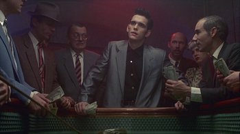 Movie still from “The Big Town” (1987), directed by Harold Becker – A group of men standing next to each other in a room; Medium shot, Low angle