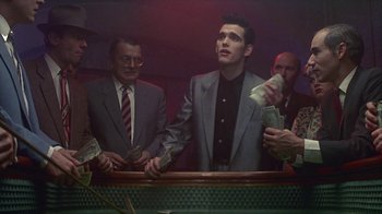 Movie still from “The Big Town” (1987), directed by Harold Becker – A group of men standing around a table; Medium shot, Low angle