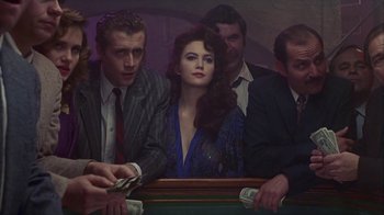 Movie still from “The Big Town” (1987), directed by Harold Becker – A group of people sitting around a table; Medium shot, High angle