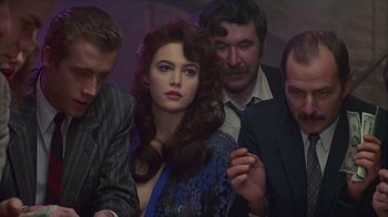 Movie still from “The Big Town” (1987), directed by Harold Becker – A group of men standing around a beautiful woman; Medium shot, Over the shoulder angle