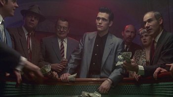 Movie still from “The Big Town” (1987), directed by Harold Becker – A group of men standing around a table with money; Medium shot, Low angle