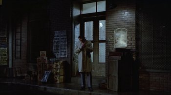 Movie still from “The Big Town” (1987), directed by Harold Becker – A man standing in front of a building at night; Wide shot, High angle