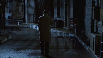 Movie still from “The Big Town” (1987), directed by Harold Becker – A man standing in the rain holding a gun; Wide shot, High angle