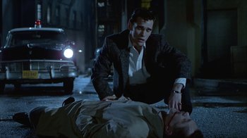 Movie still from “The Big Town” (1987), directed by Harold Becker – A man in a business suit is kneeling over another man; Medium shot, Low angle