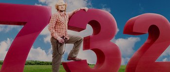 Movie still from “The Big Year” (2011), directed by David Frankel – A man standing next to a large number three; Wide shot, Low angle