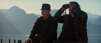 Movie still from “The Big Year” (2011), directed by David Frankel – Two men sitting on top of a hill with binoculars; Medium shot, Low angle