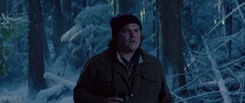 Movie still from “The Big Year” (2011), directed by David Frankel – A man in a brown jacket and a black hat holding binoculars in front of trees; Close Up shot, Low angle