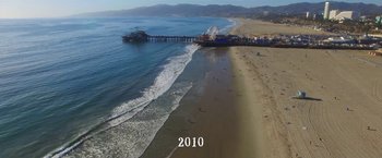 Movie still from “The Biggest Little Farm” (2018), directed by John Chester – An aerial view of a beach with a pier in the background; Extreme Wide shot, High angle